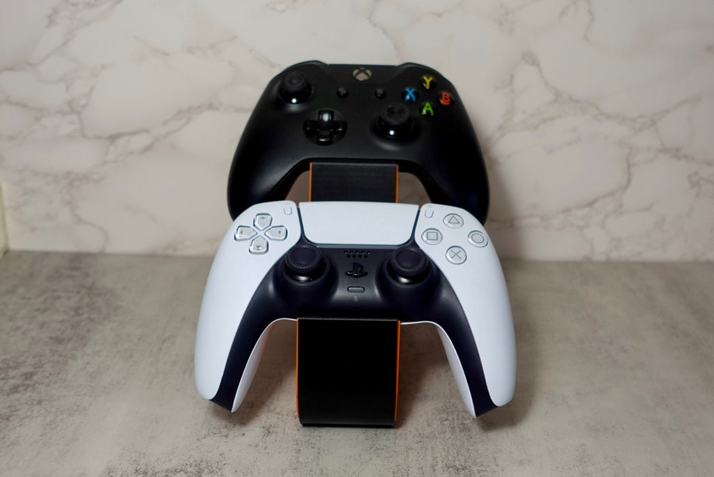 1 xbox ccontroller and 1 ps5 ccontroller placed on an orange and black holder with a honeycomb pattern on the side.