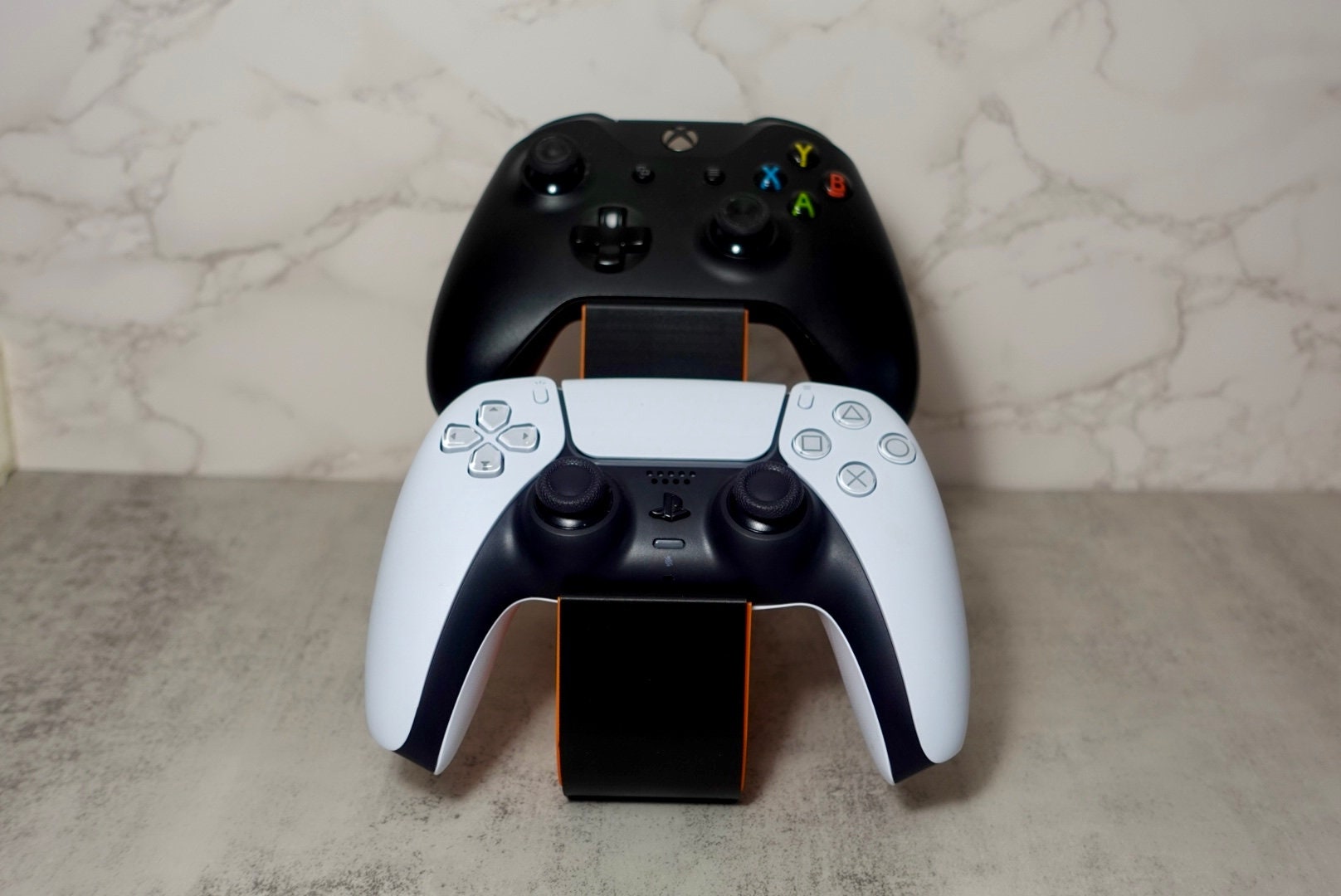 1 xbox ccontroller and 1 ps5 ccontroller placed on an orange and black holder with a honeycomb pattern on the side.