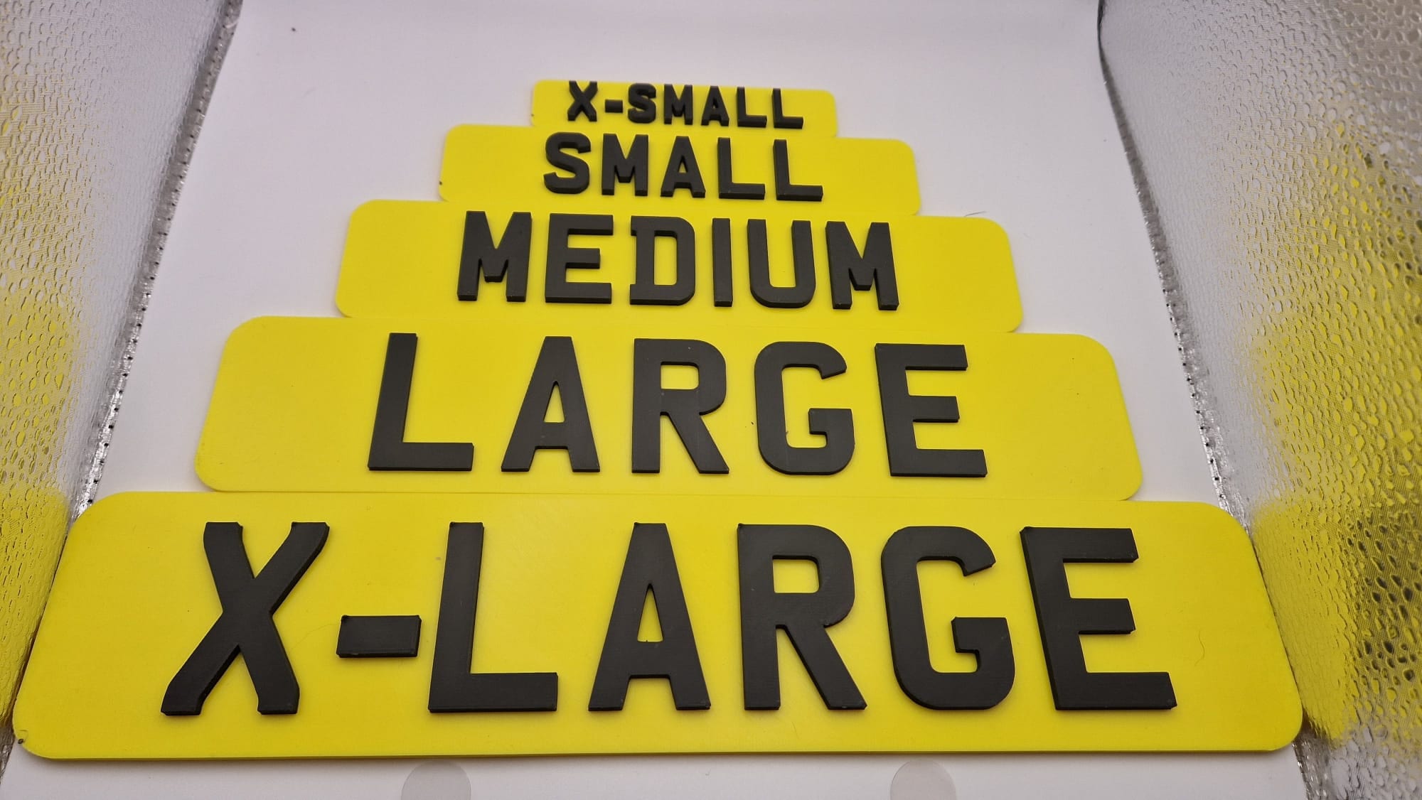 5 different sizes of registration plate available positioned next to each other, in yellow with black 3d writing